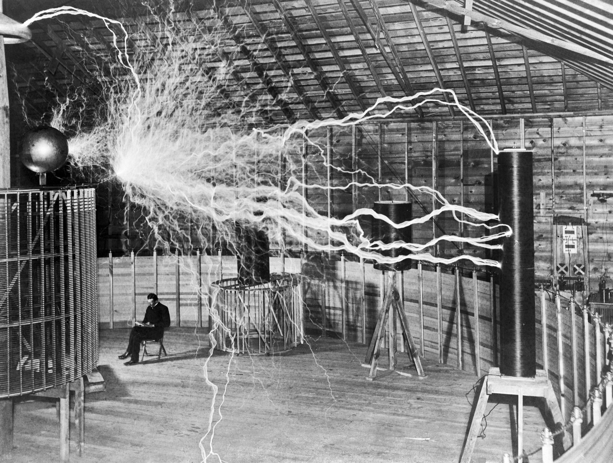 Nikola Tesla sitting in his Colorado Springs laboratory surrounded by electrical discharges